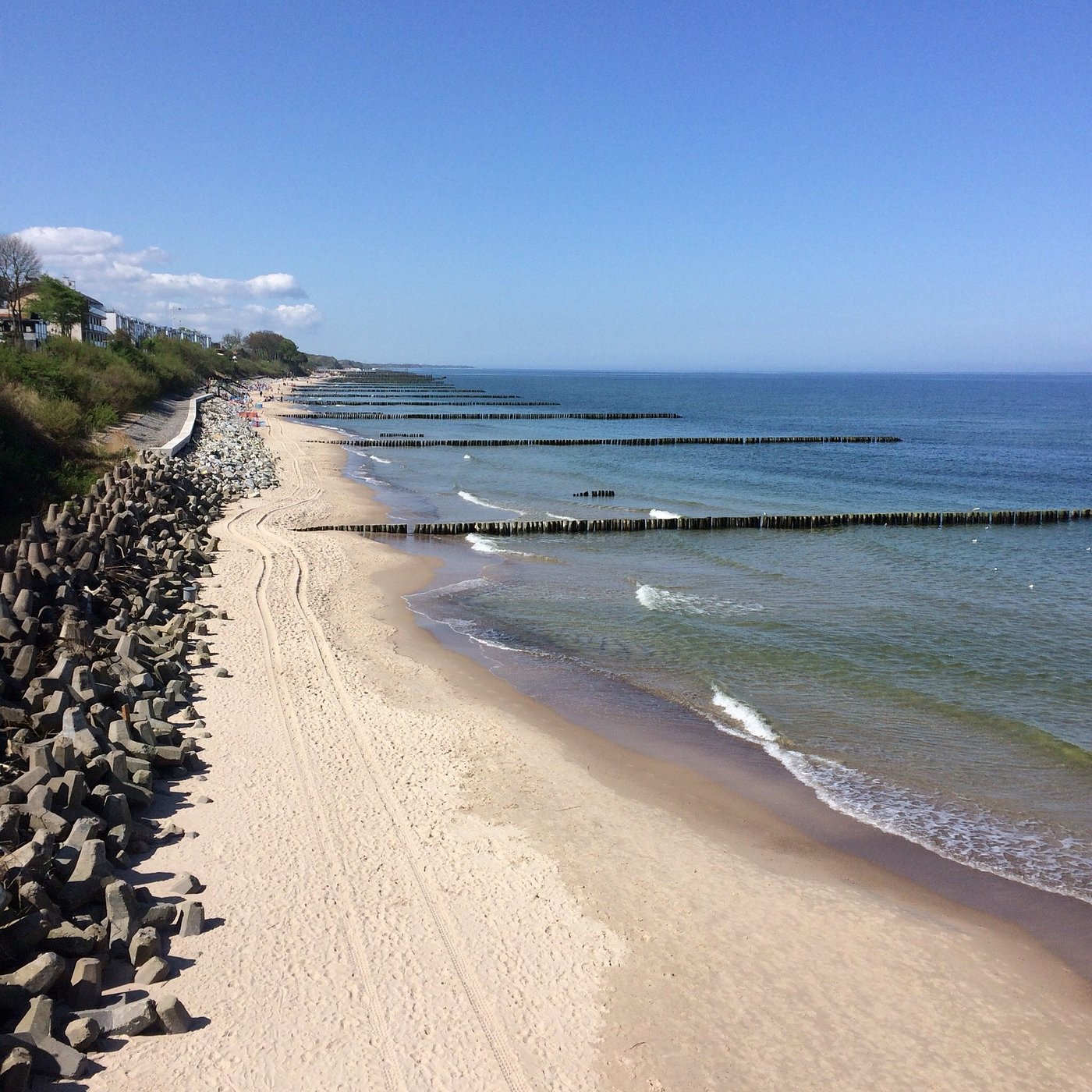 Szeroka, piaszczysta plaża w Ustroniu Morskim z falochronem i błękitnym morzem